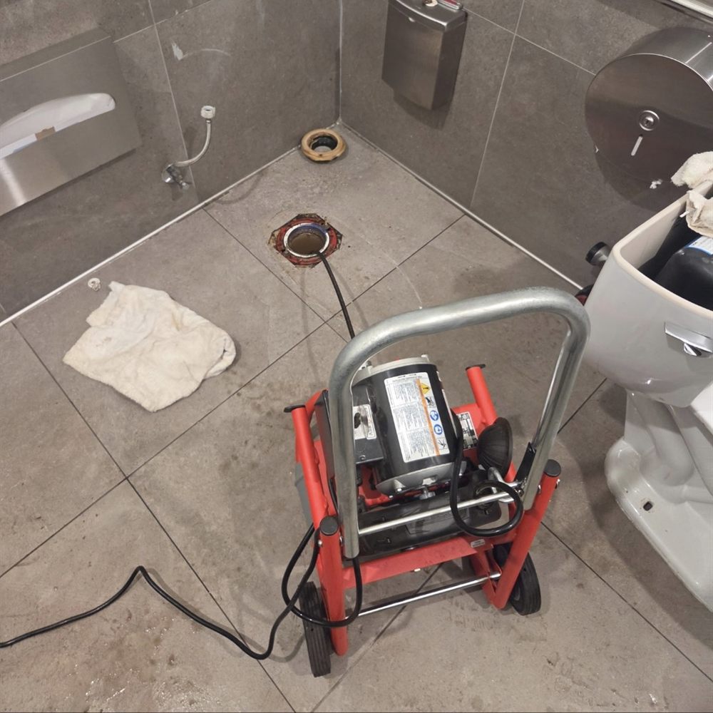 A drain machine set up in a commercial restroom with the toilet pulled