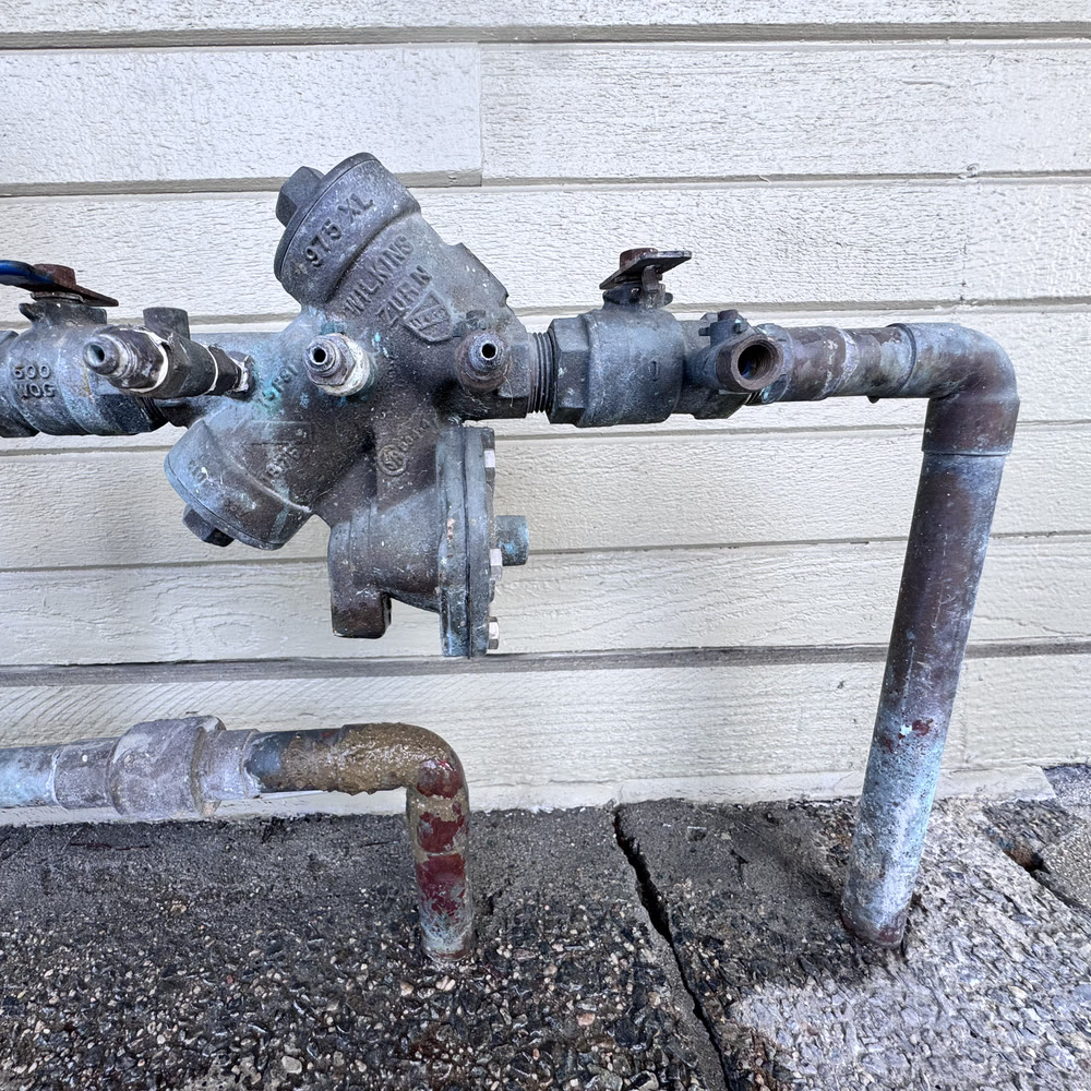 Corroded backflow assembly on an exterior wall.