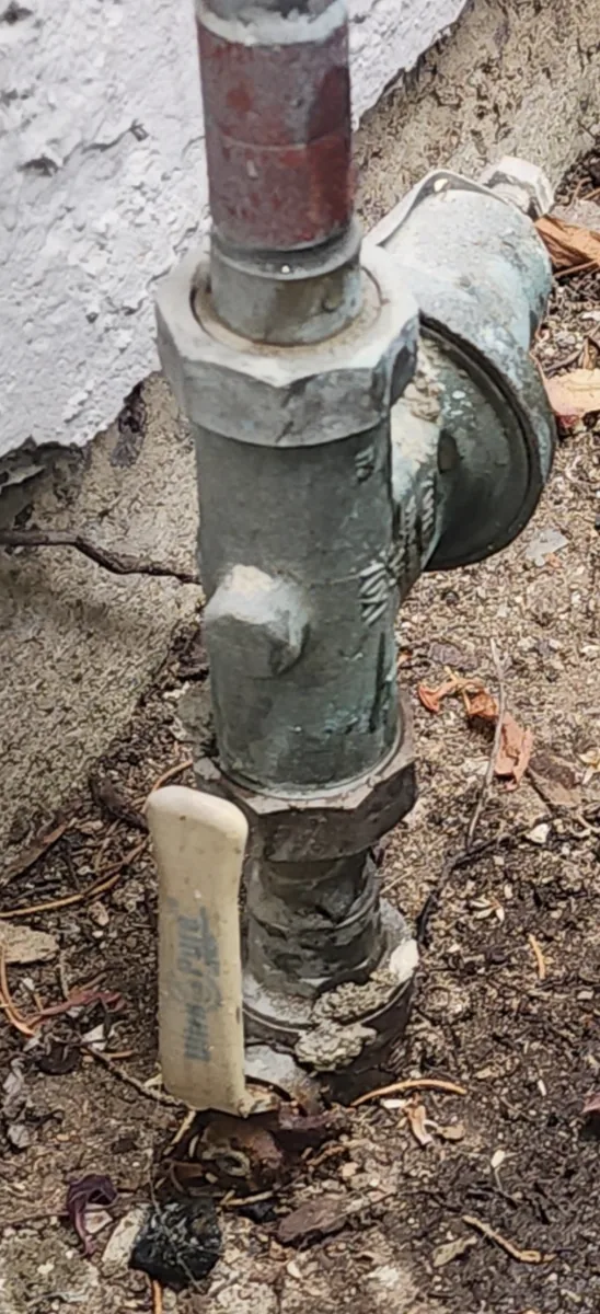 An aging water pressure regulator installed at ground level outside a home, showing corrosion on the body.