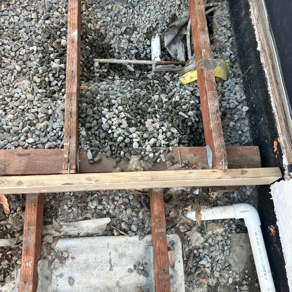Floor boards removed over gravel to reach a pipe.