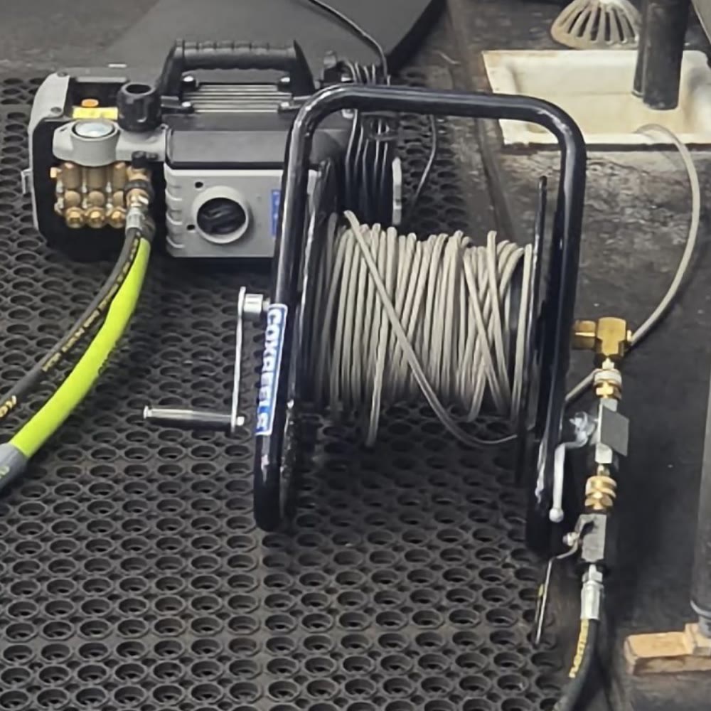 Hydro jetter with its hose reel set up on a rubber mat in a commercial kitchen