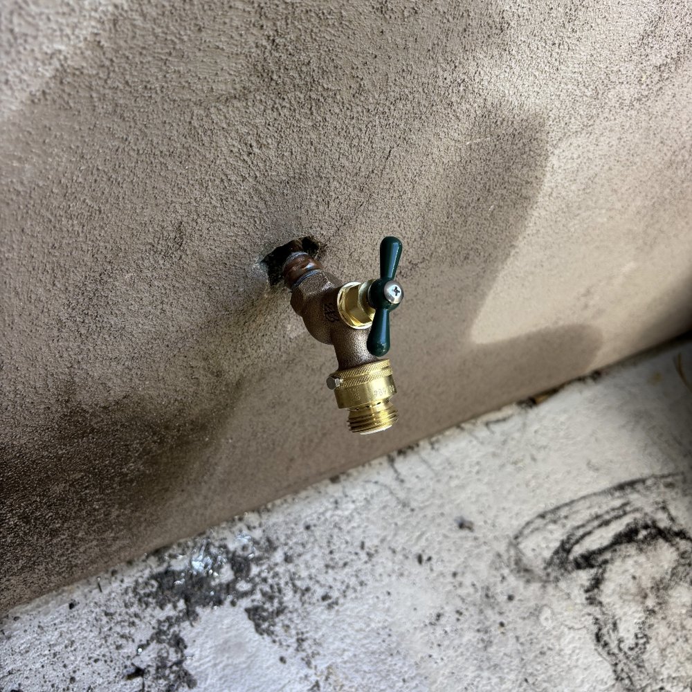 New brass hose bib on a stucco wall.