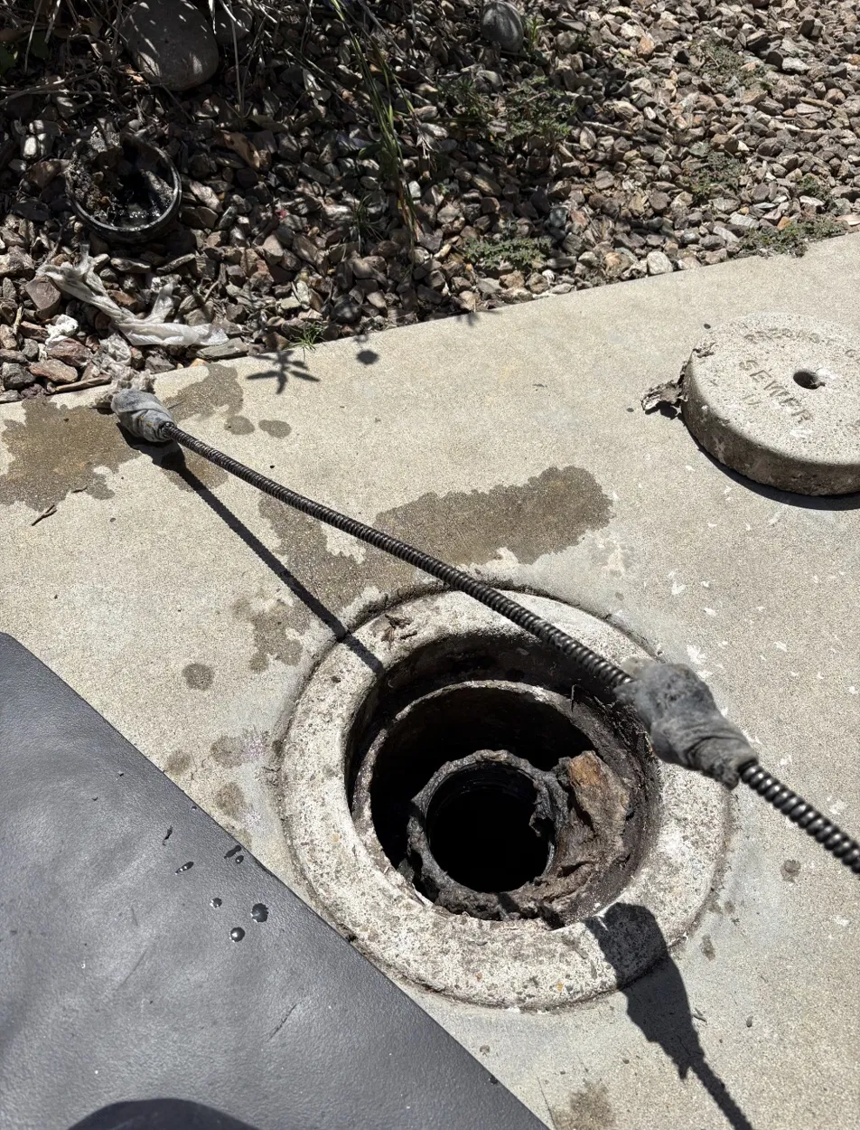 A drain cleaning machine set up on a walkway with its cable running into an open sewer cleanout.