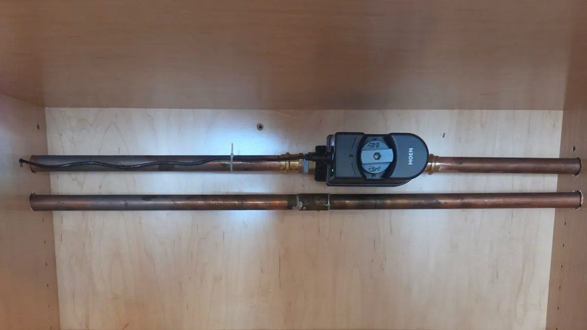 A smart water shutoff installed inline on copper pipe inside a cabinet.