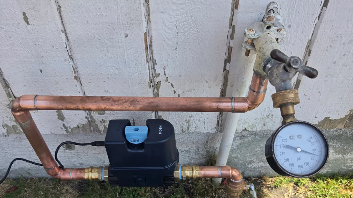 A smart water shutoff mounted on the water line at the exterior wall of a home.