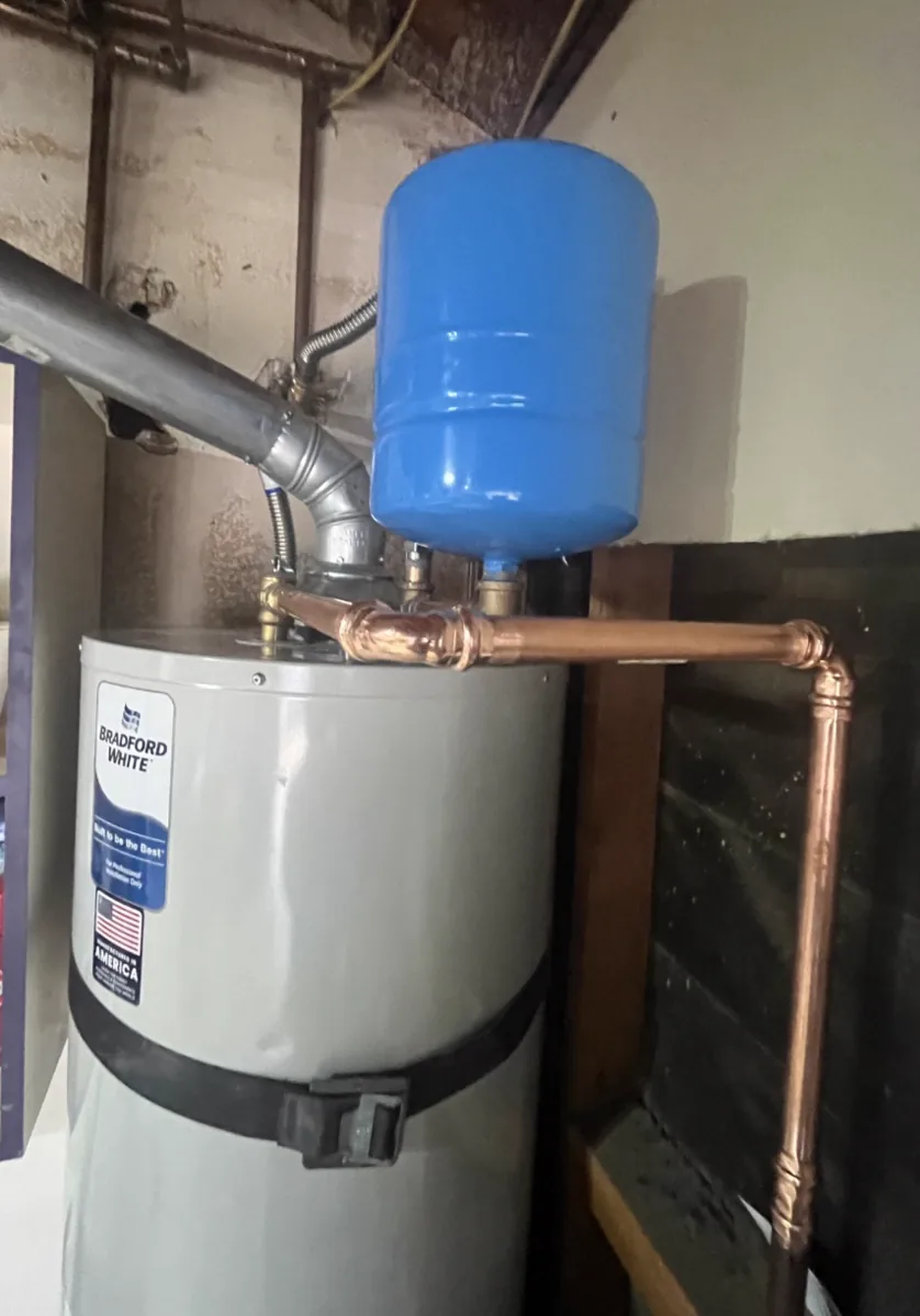 A blue thermal expansion tank installed on the cold water line above a residential water heater.