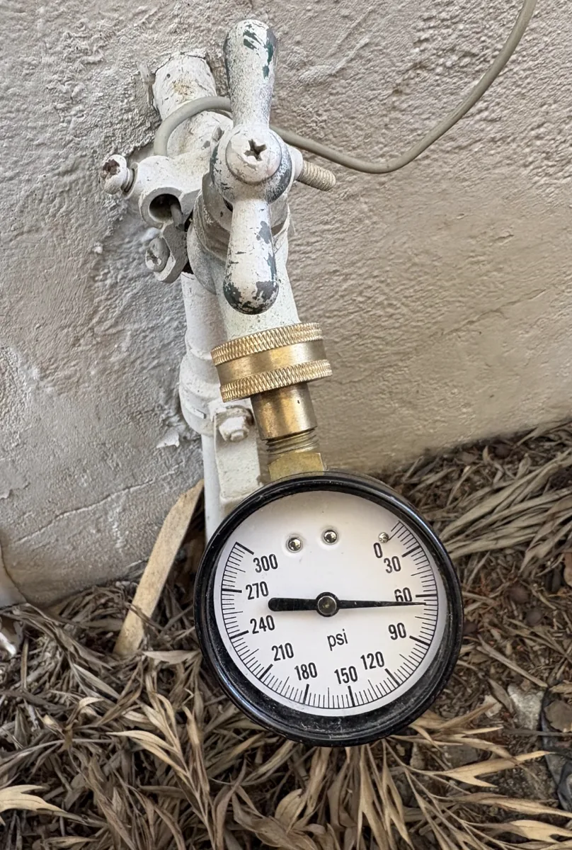 A pressure test gauge threaded onto an outdoor hose bib at a home.